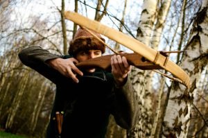 Un homme en vêtements médiévaux vise une arbalète dans une forêt, représentant une reconstitution historique.