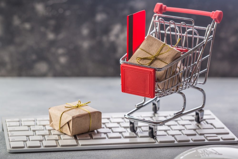 Un mini-chariot de courses contenant un cadeau et une carte, posé sur un clavier, évoquant le shopping en ligne Temu.