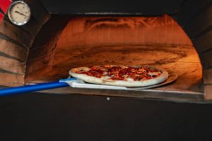 Une pizza en cours de cuisson sur une pelle dans un four à pizza traditionnel en brique