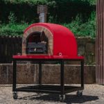 Un four à pizza extérieur rouge et moderne monté sur un support noir à roulettes.