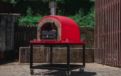 Un four à pizza extérieur rouge et moderne monté sur un support noir à roulettes.