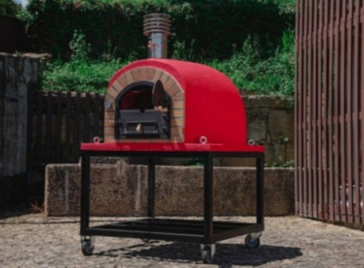 Un four à pizza extérieur rouge et moderne monté sur un support noir à roulettes.