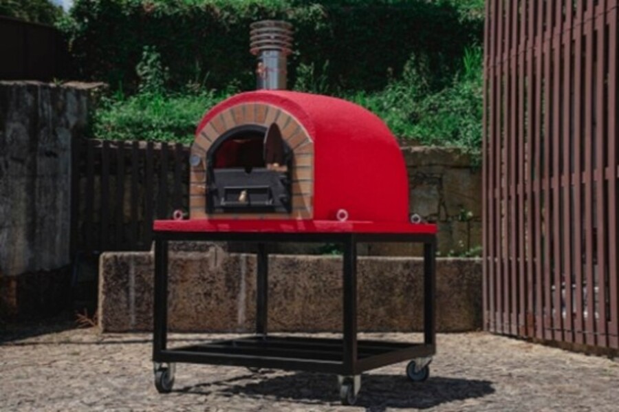 Un four à pizza extérieur rouge et moderne monté sur un support noir à roulettes.